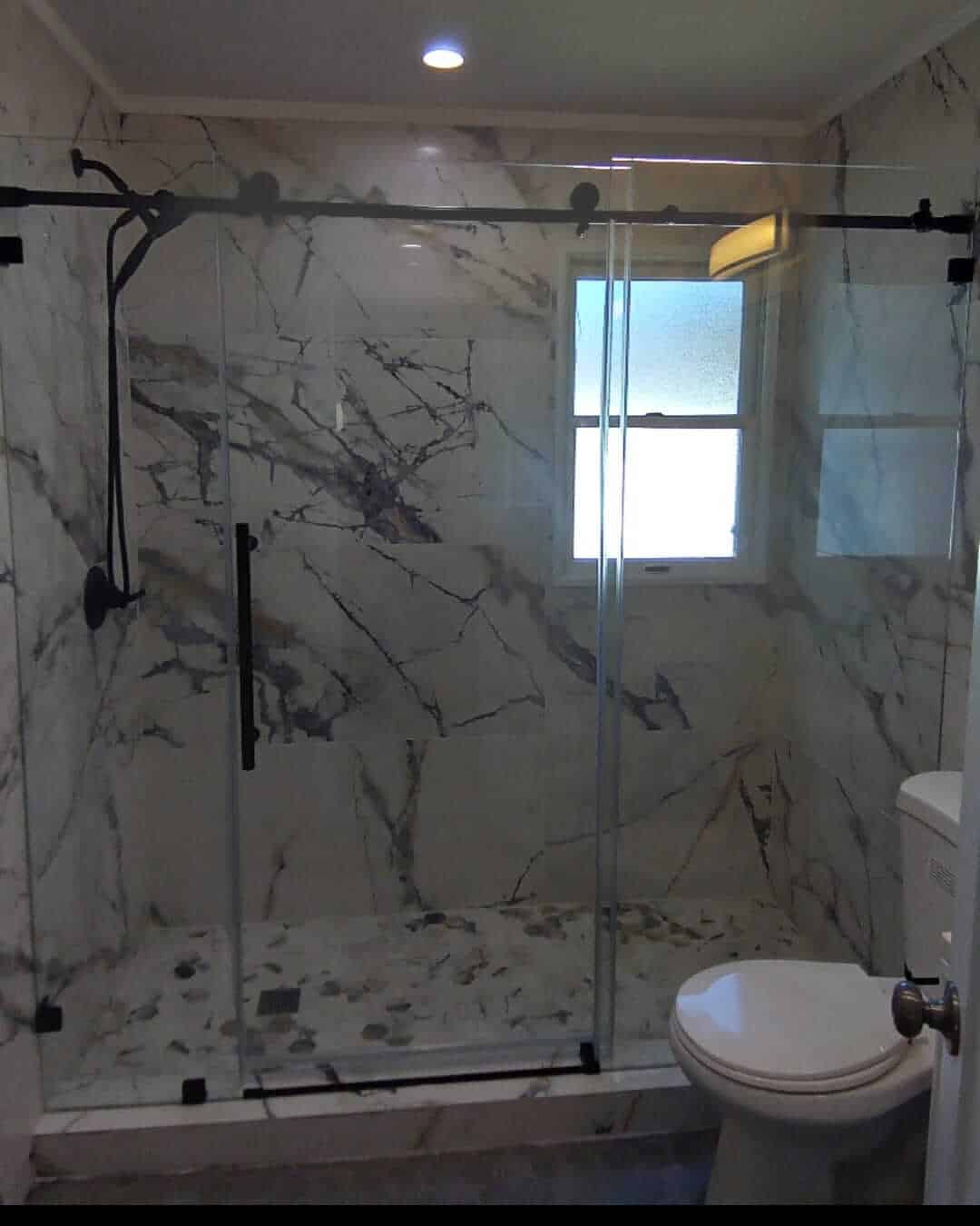 Elegant glass shower door with black hardware in marble-tiled bathroom. Frameless Glass Shower Doors vs Framed Shower Doors: What’s the Difference?