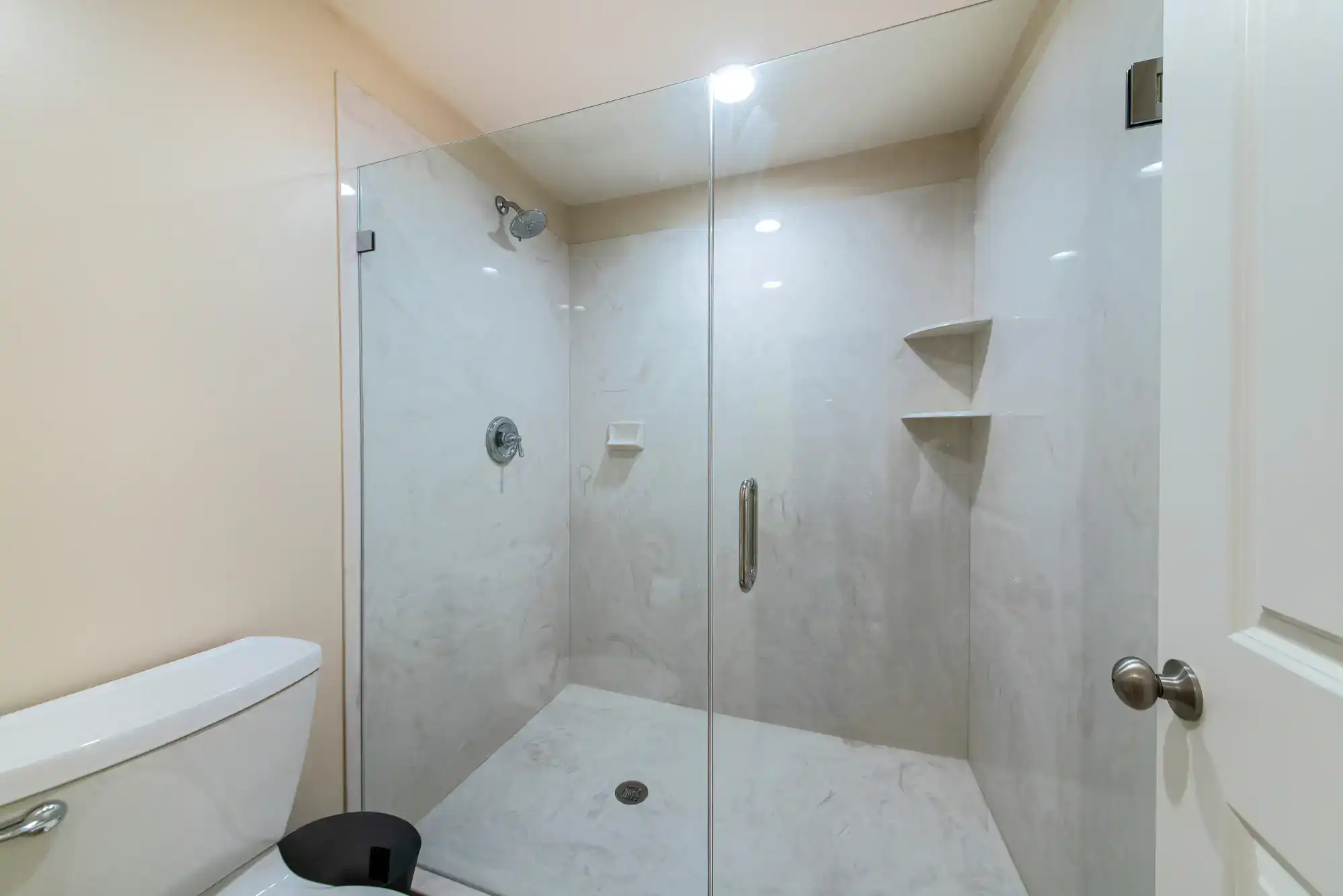 Shower door with clear glass, stainless steel handle, and built-in corner shelves for contemporary bathroom design.