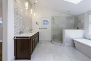 OMG Shower Doors Is Stepping Up: The Thrilling Future of Bathroom Remodeling | OMG Shower Doors Modern bathroom with white marble tile, dark wood double vanity, two sinks, mosaic accent wall, glass-enclosed shower, and a white freestanding bathtub next to a window. Pendant lights hang above the vanity.